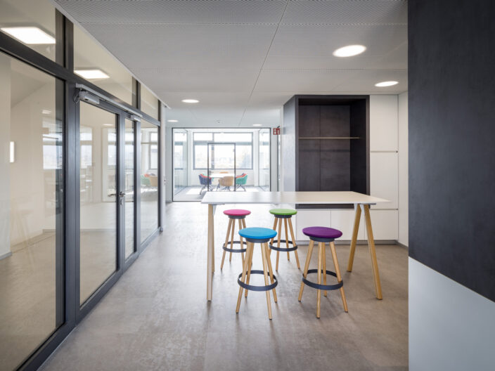 Innenperspektive Büroräumlichkeiten mit offenen Kommunikationszonen und verglasten Meetingräumen im Neubau der Firma PLC2 Design