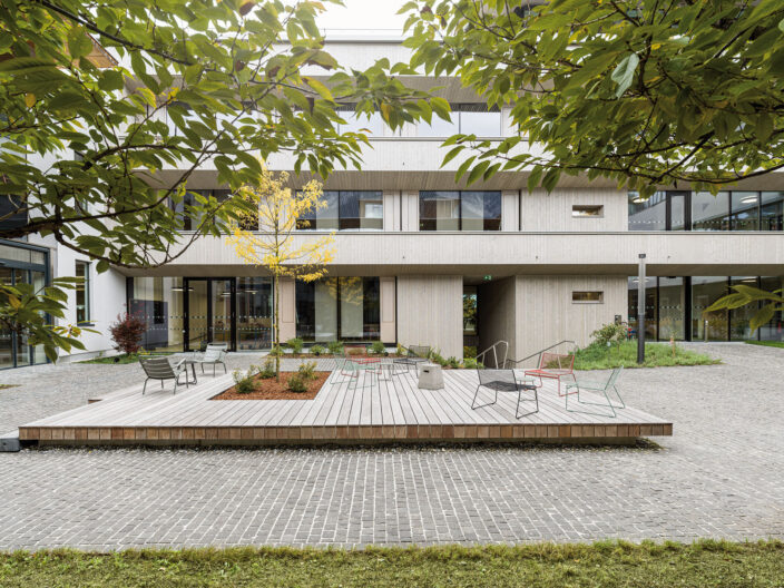 Außenperspektive Innenhof mit Holzterrasse und Sitzmöglichkeiten Umgeben von Begrünung der Swarovski Optik Verwaltung und Produktion